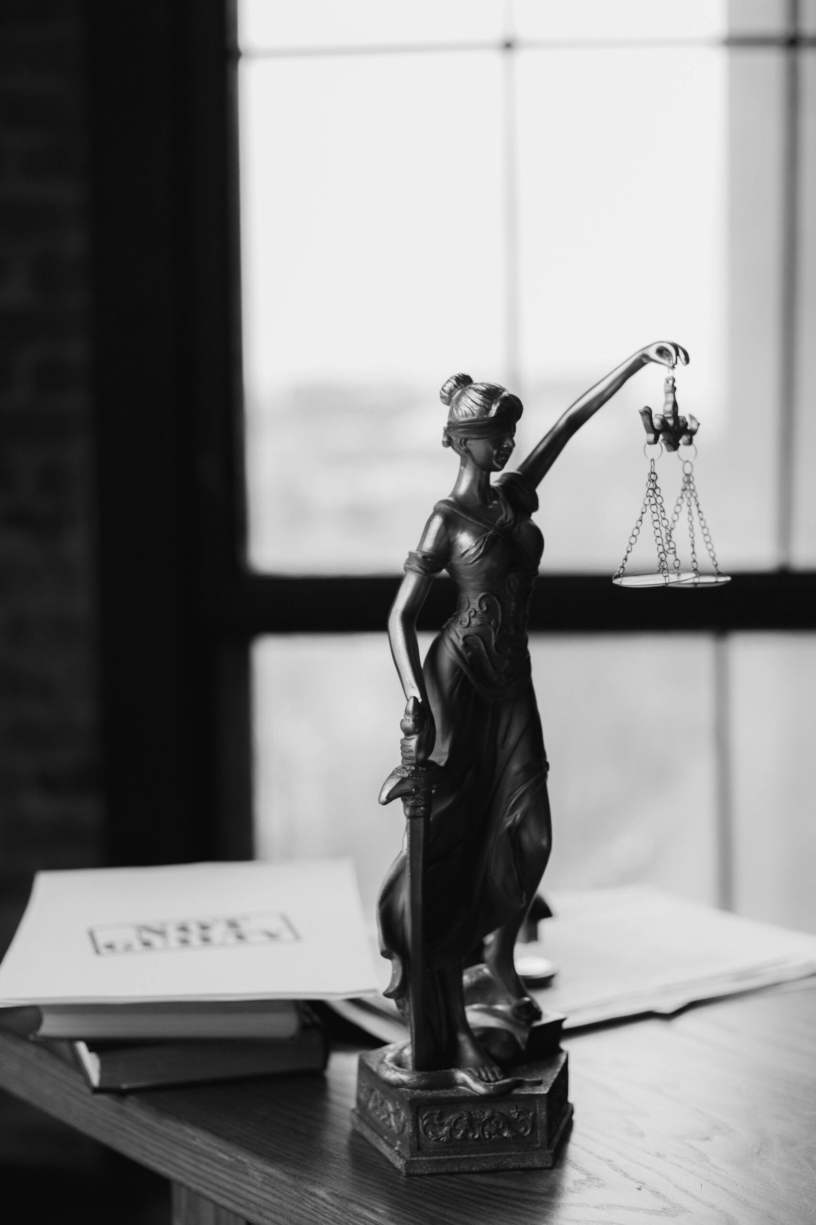 Elite Investigation & Protection for Legal Professionals, Insurance Carriers, and Private Individuals. Grayscale photo of Lady Justice statue beside legal documents on a wooden table.